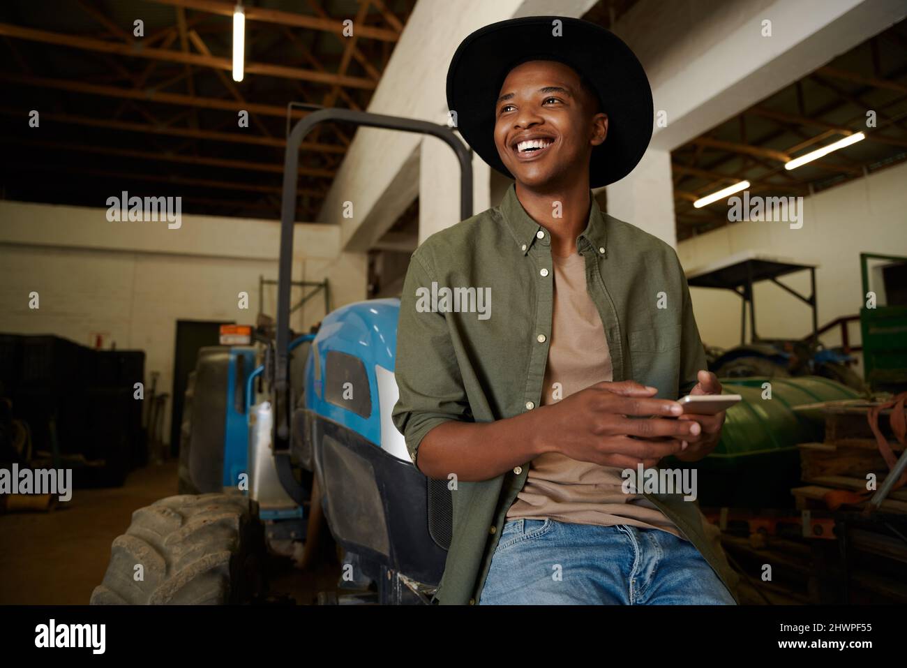sorridente agricoltore misto razza maschile seduto sul trattore sms su dispositivo cellulare Foto Stock