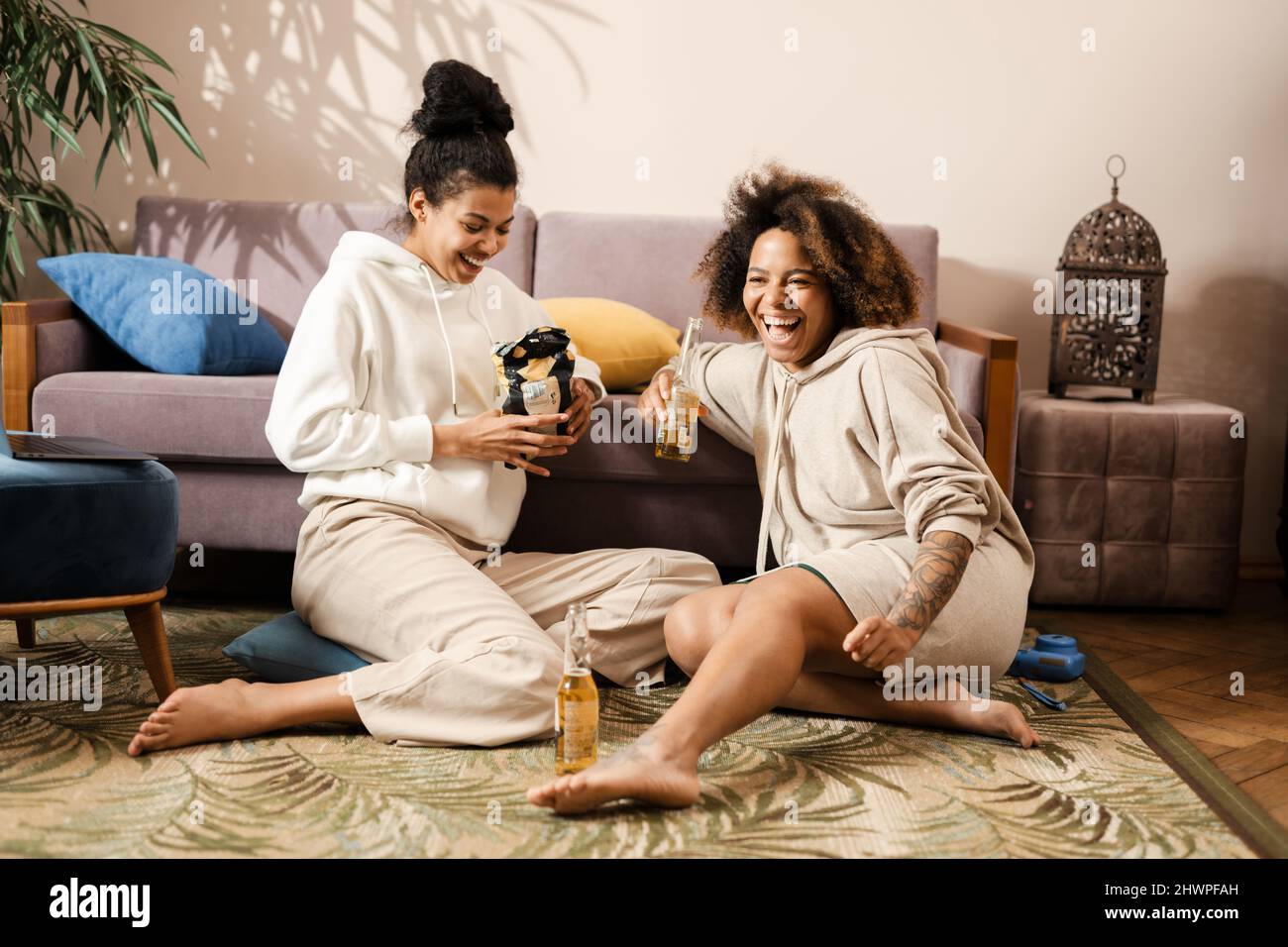 Tre allegre donne multietniche amici seduti su un divano a casa con spuntini guardando la TV Foto Stock