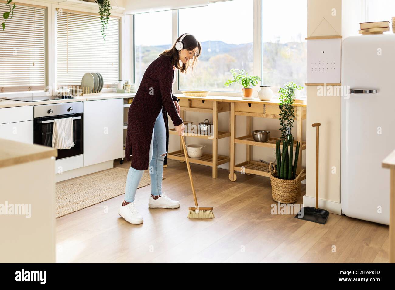 Giovane donna pulizia piano cucina con scopa a casa Foto Stock