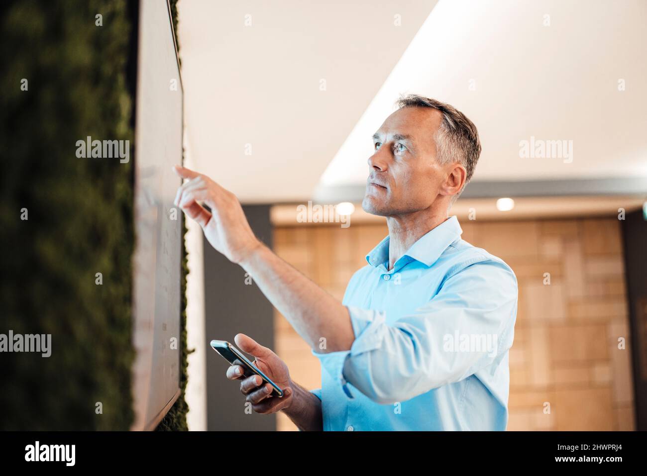 Uomo d'affari che punta al monitor del calcolatore del touch screen nell'ufficio di collegio Foto Stock