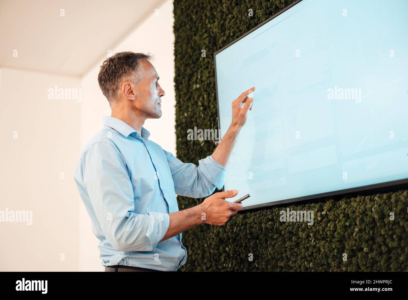 Uomo d'affari maturo che punta al monitor del calcolatore dello schermo a sfioramento nell'ufficio di collegio Foto Stock