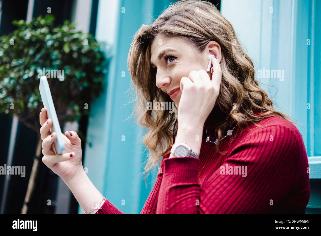 Donna sorridente con smartphone che regola le cuffie bluetooth Foto Stock