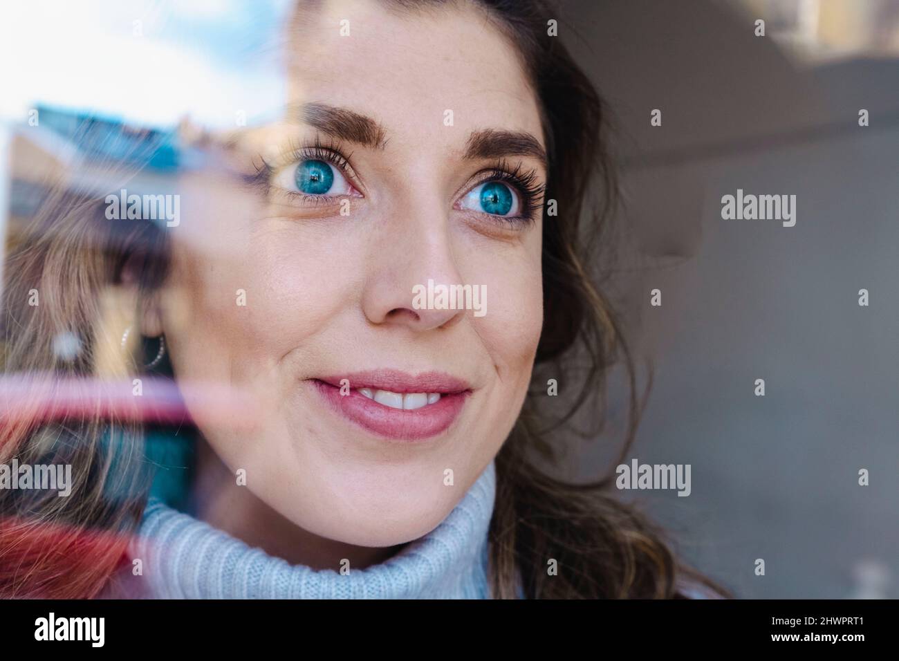 Donna pensierosa con occhi blu visti attraverso il vetro Foto Stock