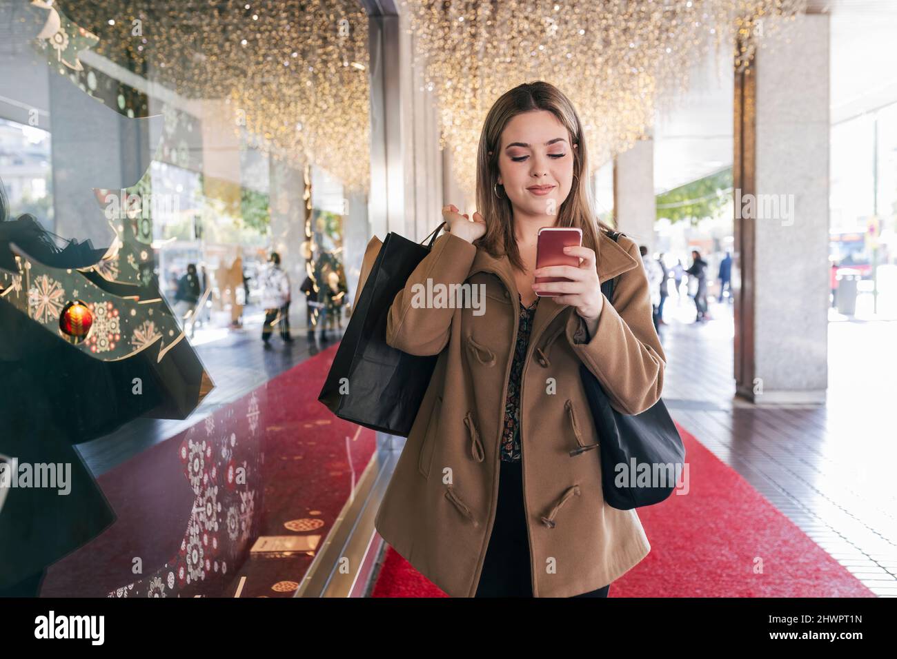 Sorridendo con i sacchetti di shopping usando il telefono mobile dal deposito a Natale Foto Stock