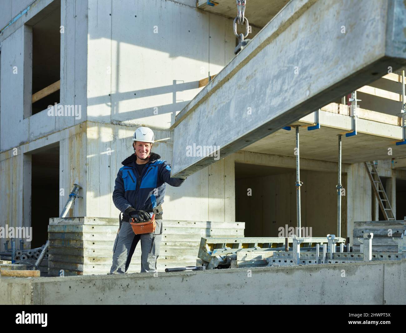 Sorridente lavoratore in piedi vicino a materiale da costruzione in loco Foto Stock