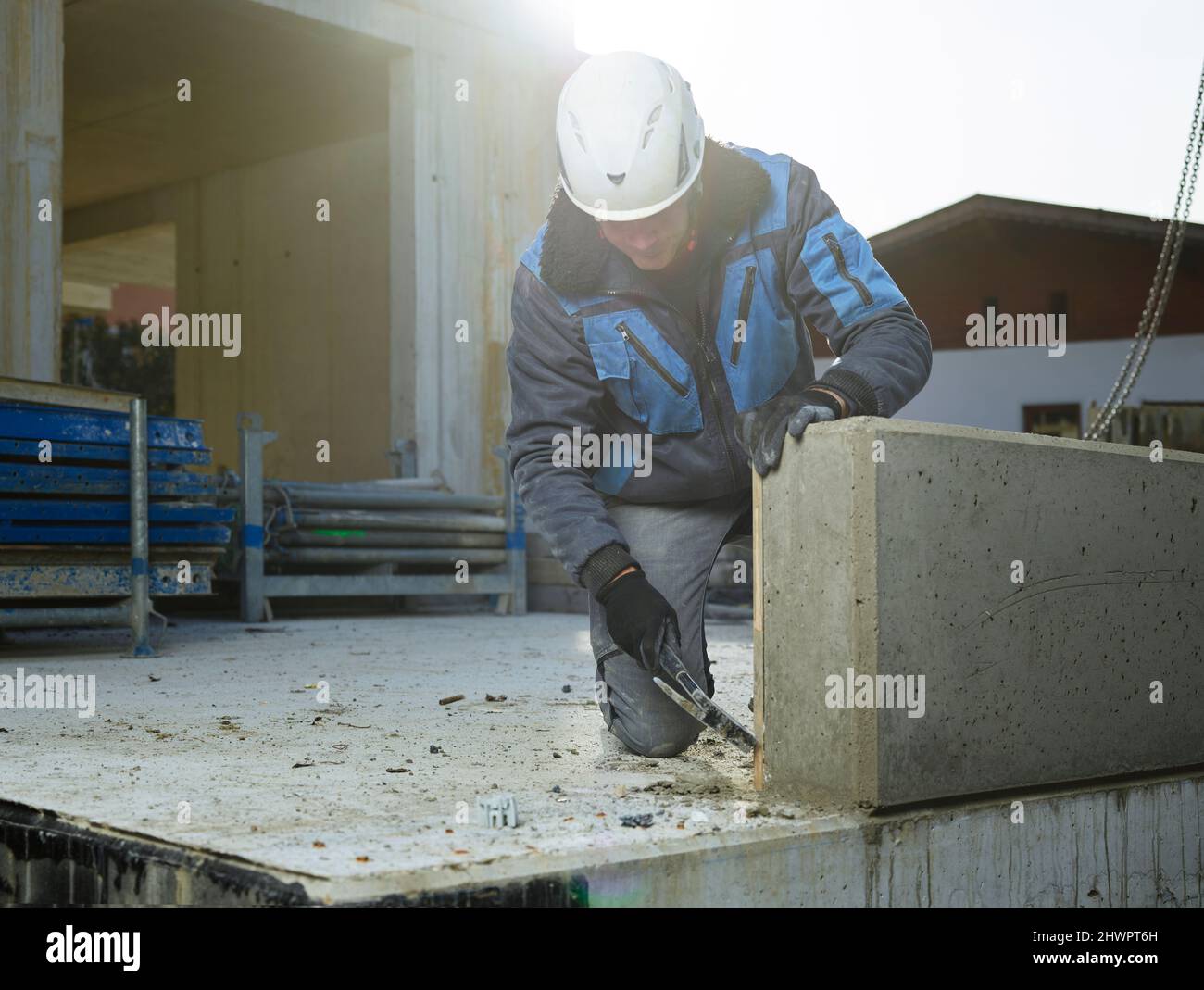 L'angolo di pulizia del lavoratore della lastra di cemento con il martello inginocchiato in cantiere Foto Stock