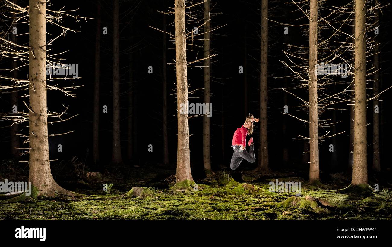 Donna attiva che salta nella foresta di notte Foto Stock