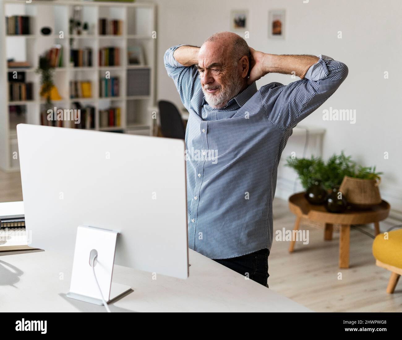 Uomo d'affari anziano con le mani dietro la testa che guarda il computer in ufficio domestico Foto Stock