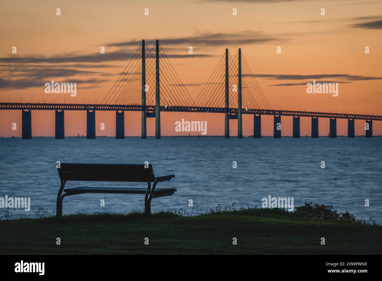 Svezia, Skane County, Malmo, Oresund Bridge al tramonto con panchina vuota in primo piano Foto Stock