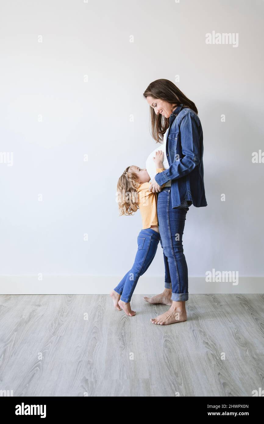 Madre incinta con figlia in piedi accanto al muro Foto Stock