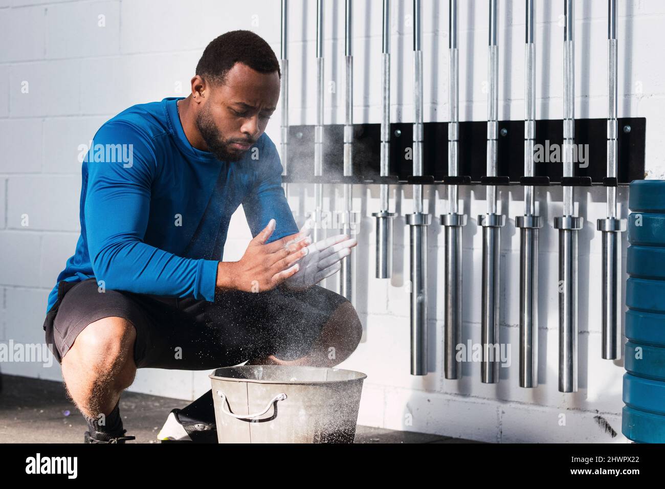 L'atleta che applica la polvere di gesso accovacciando vicino al secchio in palestra Foto Stock