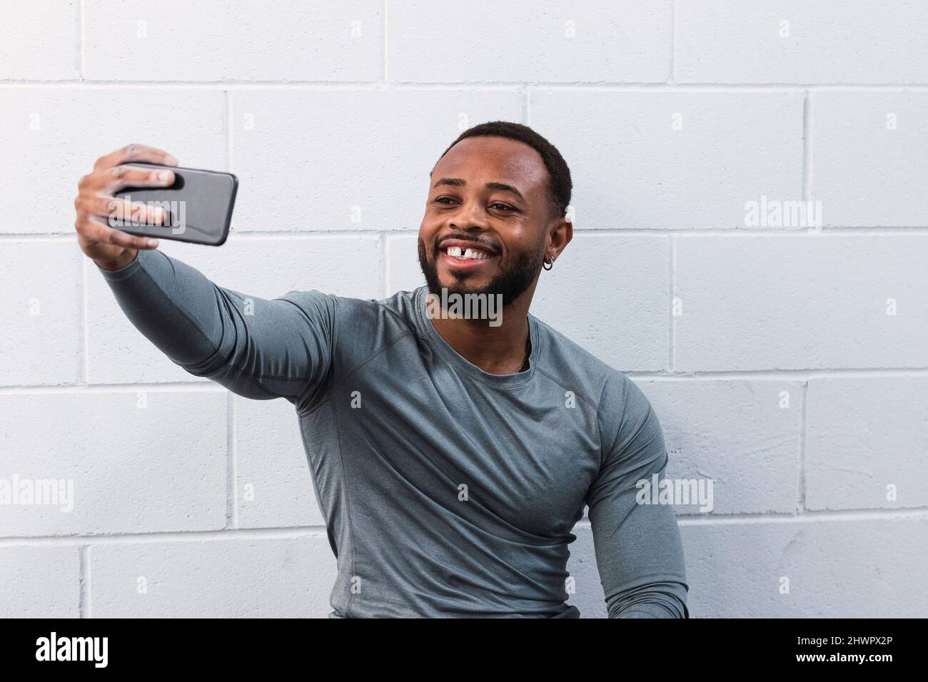 Un atleta sorridente con denti a fessura che porta i selfie attraverso lo smartphone davanti alla parete Foto Stock
