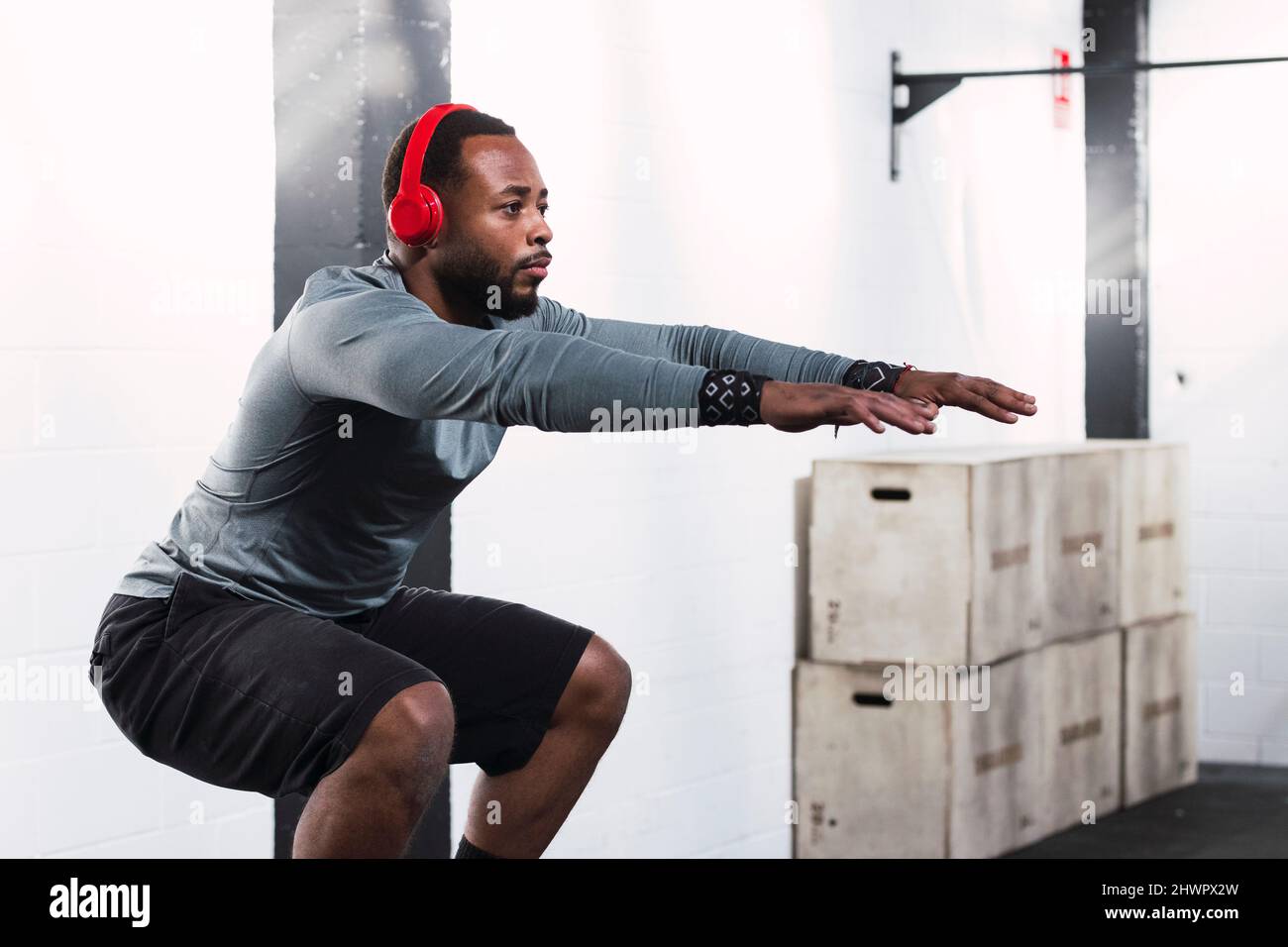 Atleta con cuffie che praticano squat in palestra Foto Stock