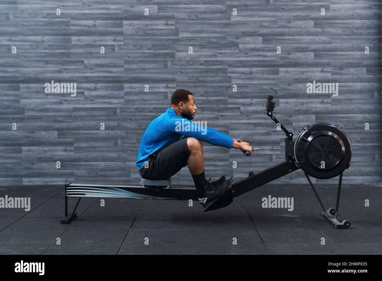 Atleta concentrato che si esercita sulla voga di fronte al muro in palestra Foto Stock