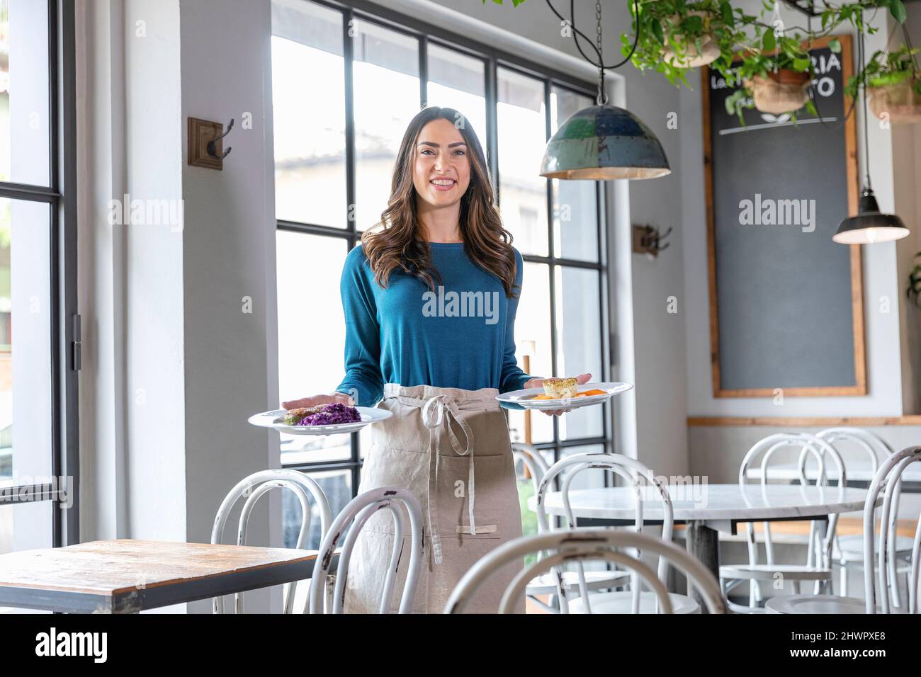 Cameriera sorridente con piatti da cucina che lavorano al bar Foto Stock