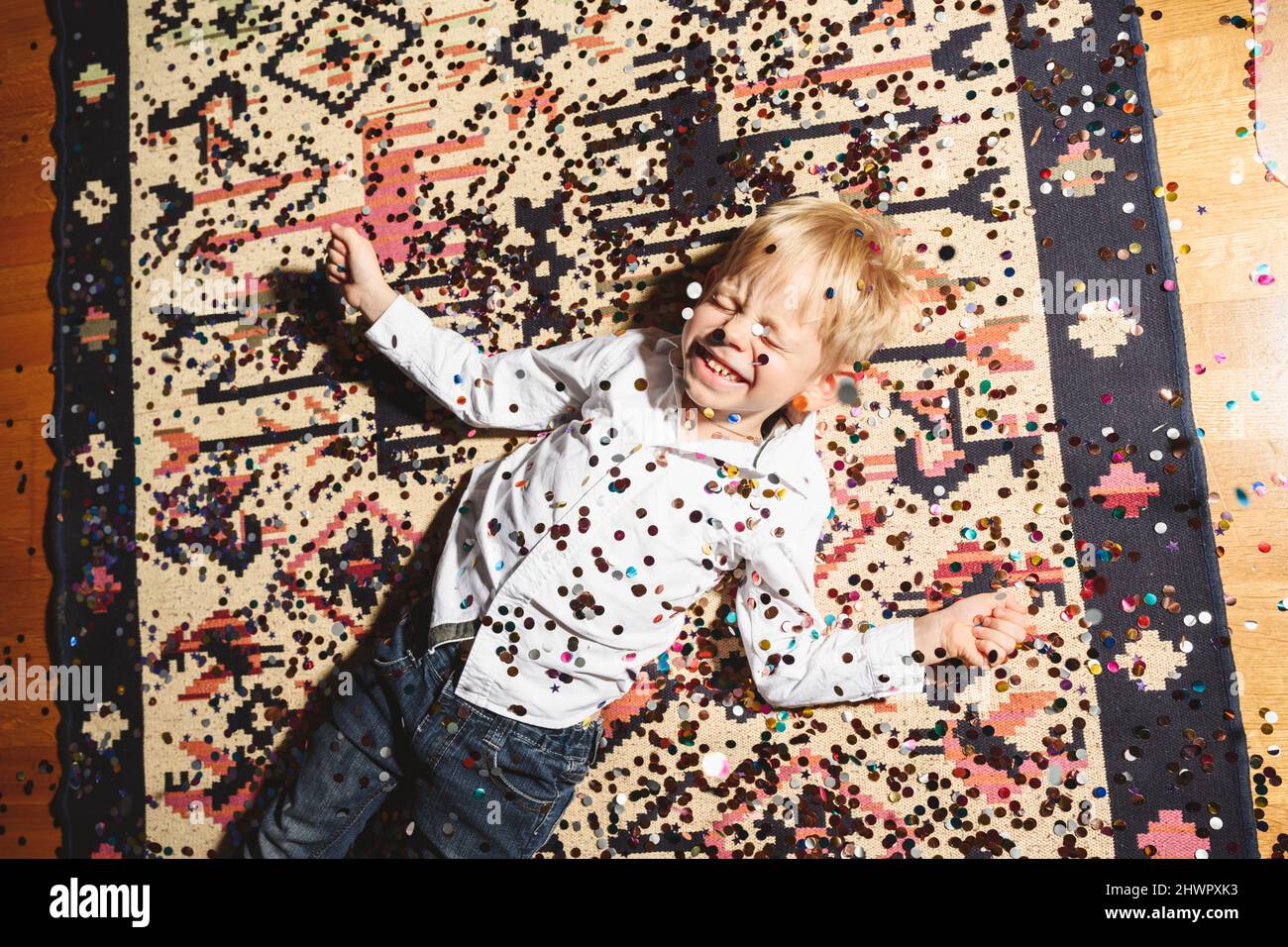 Ragazzo allegro giacente sul pavimento coperto di confetti Foto Stock