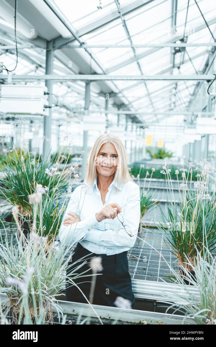 Agronomo sorridente in piedi tra piante al centro giardino Foto Stock