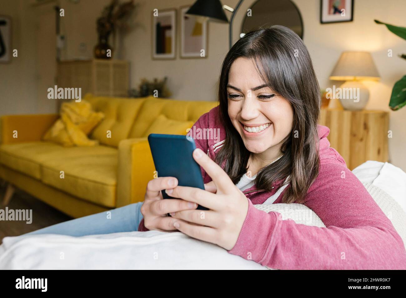 Messaggi di testo per donna felice tramite smartphone in salotto Foto Stock