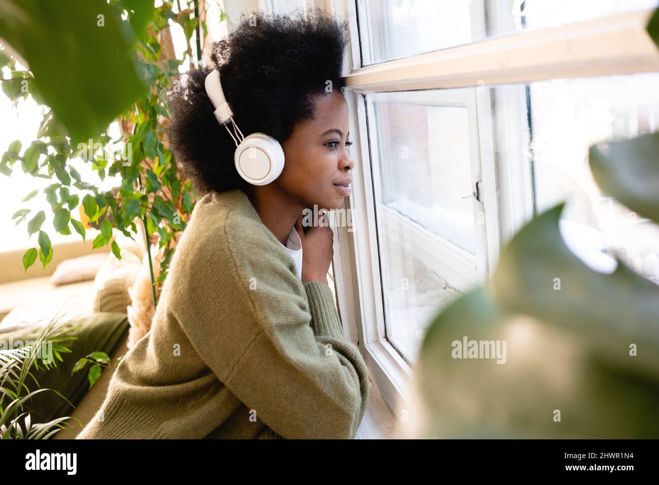 Giovane donna che ascolta musica e guarda attraverso la finestra a casa Foto Stock