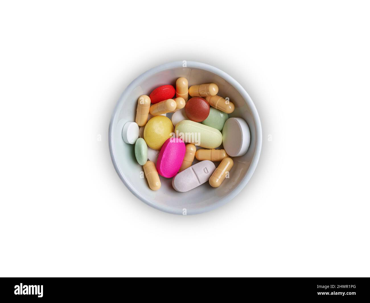 Una ciotola bianca di varie pillole colorate e capsule isolate su sfondo bianco. Foto Stock