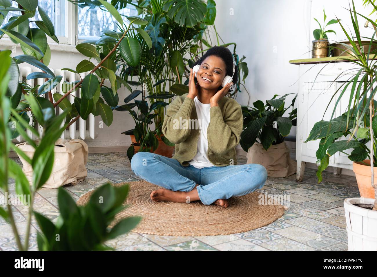 Donna sorridente che ascolta la musica attraverso le cuffie sul tappeto a casa Foto Stock