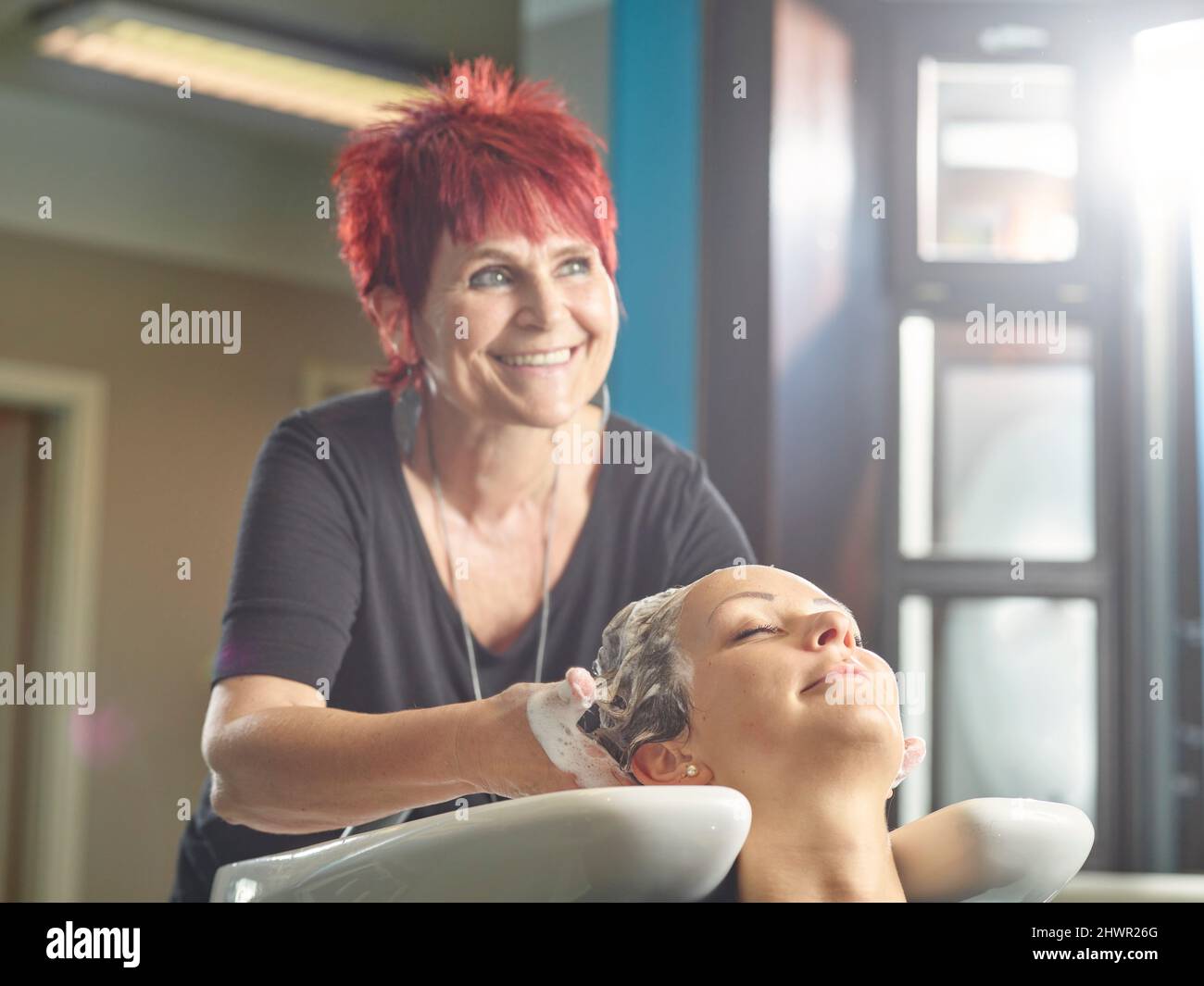 Felice parrucchiere lavaggio capelli donna in salone Foto Stock