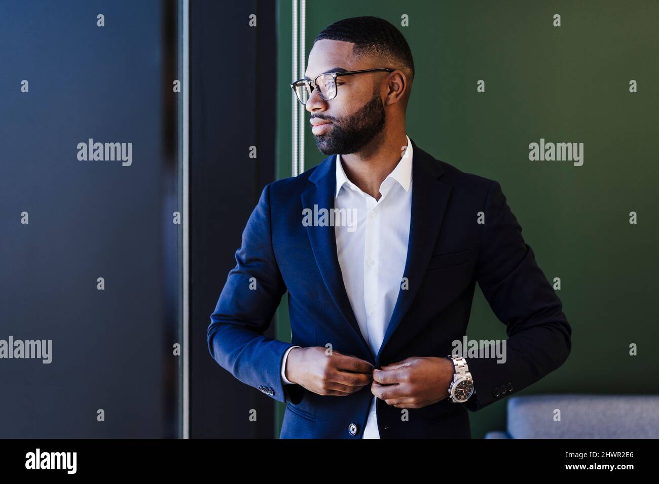 Un uomo d'affari contemplativo che regola il blazer in ufficio Foto Stock