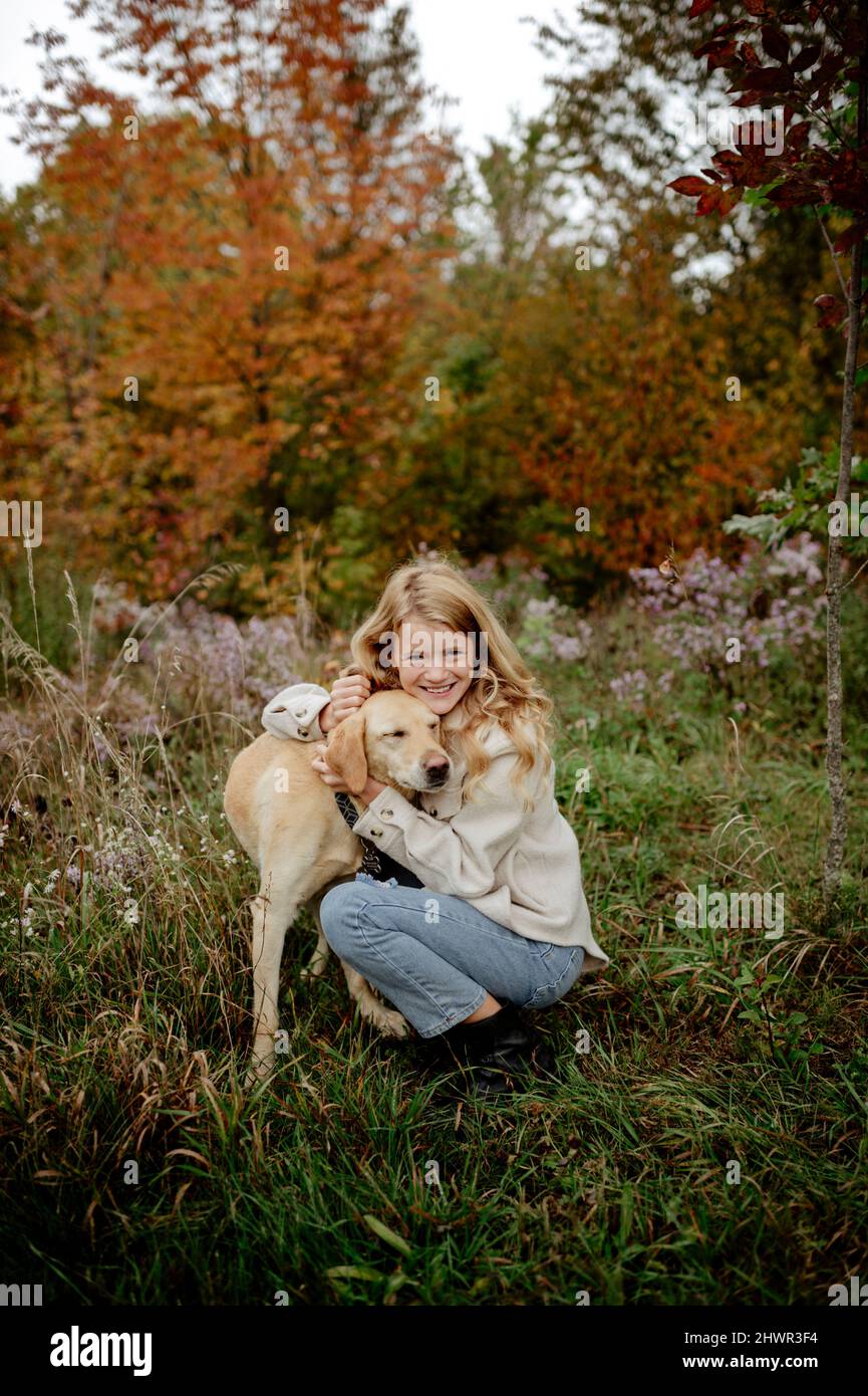 Sorridente ragazza bionda abbracciante cane da compagnia in giardino Foto Stock