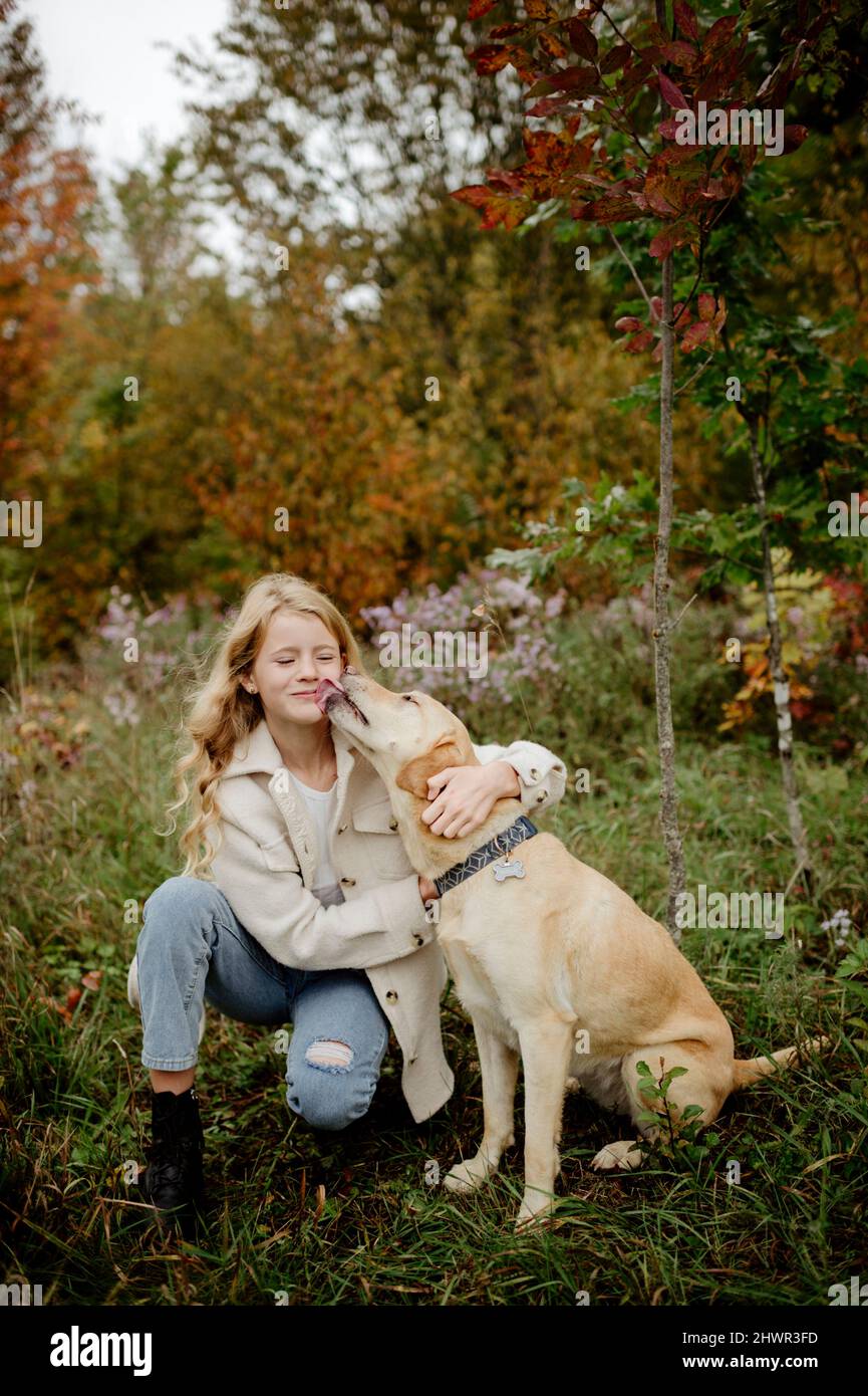 Cane che lecca la faccia della ragazza bionda in giardino Foto Stock