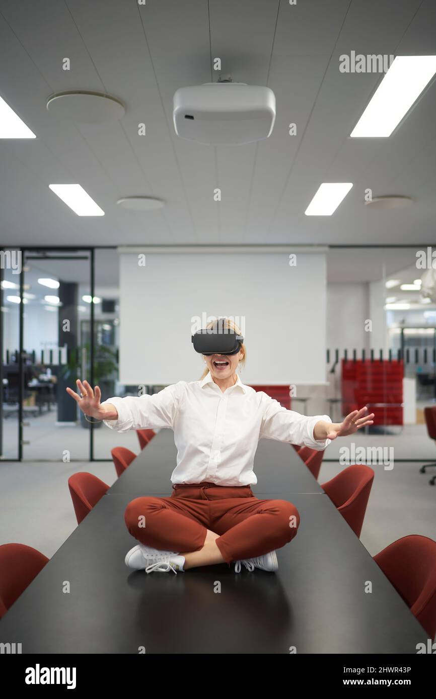 Donna d'affari allegra che indossa occhiali VR seduti nella sala riunioni dell'ufficio Foto Stock