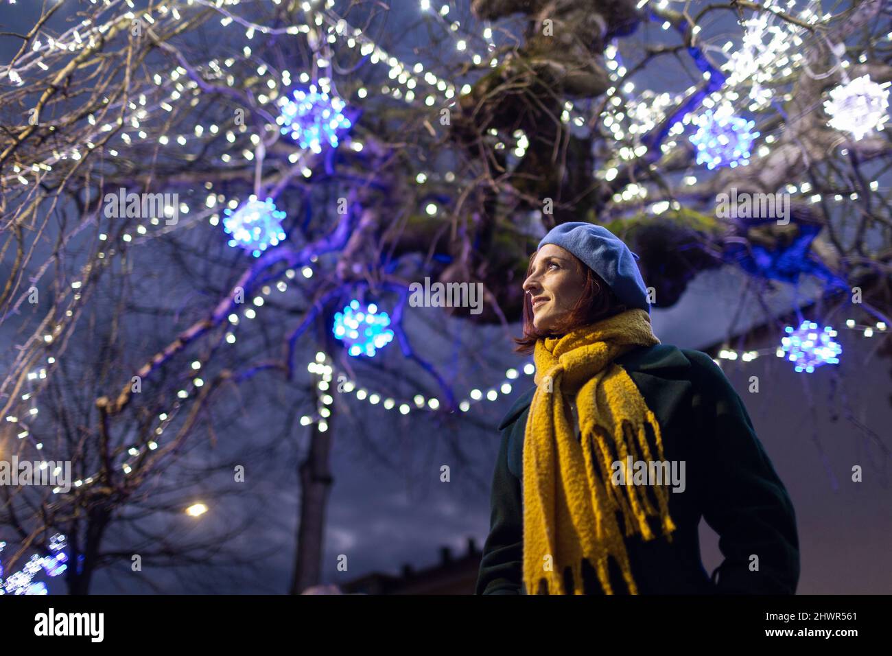 Donna che indossa sciarpa gialla in piedi sotto l'albero illuminato Foto Stock
