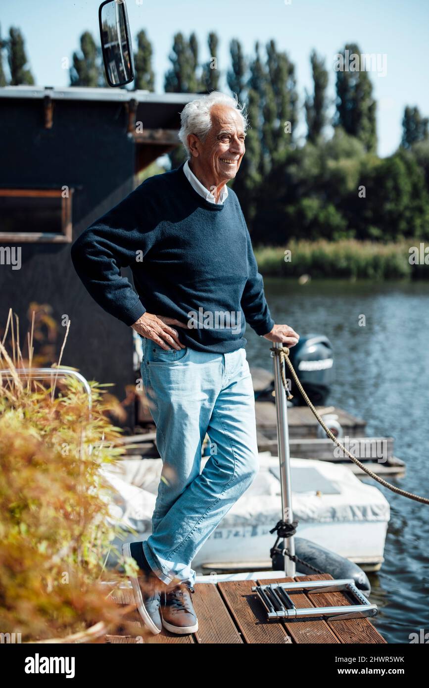 Uomo anziano felice con mano su fianco in piedi a houseboat Foto Stock
