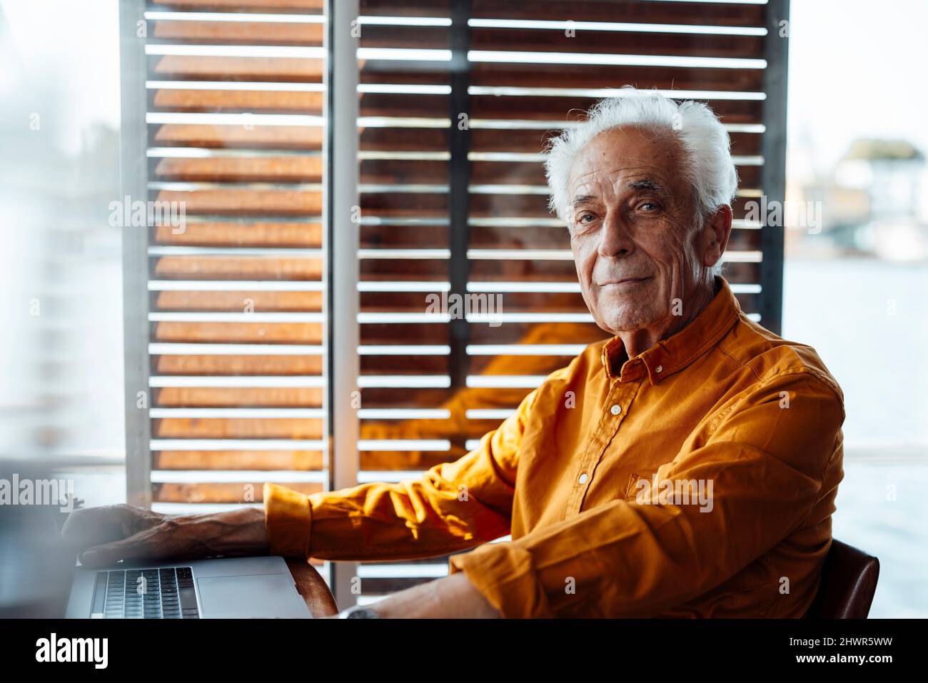 Uomo anziano seduto con un computer portatile in casa galleggiante Foto Stock