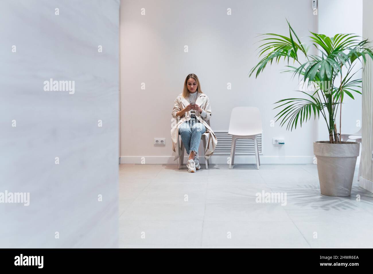 Giovane donna che usa il telefono cellulare seduto in sala d'attesa presso la clinica Foto Stock