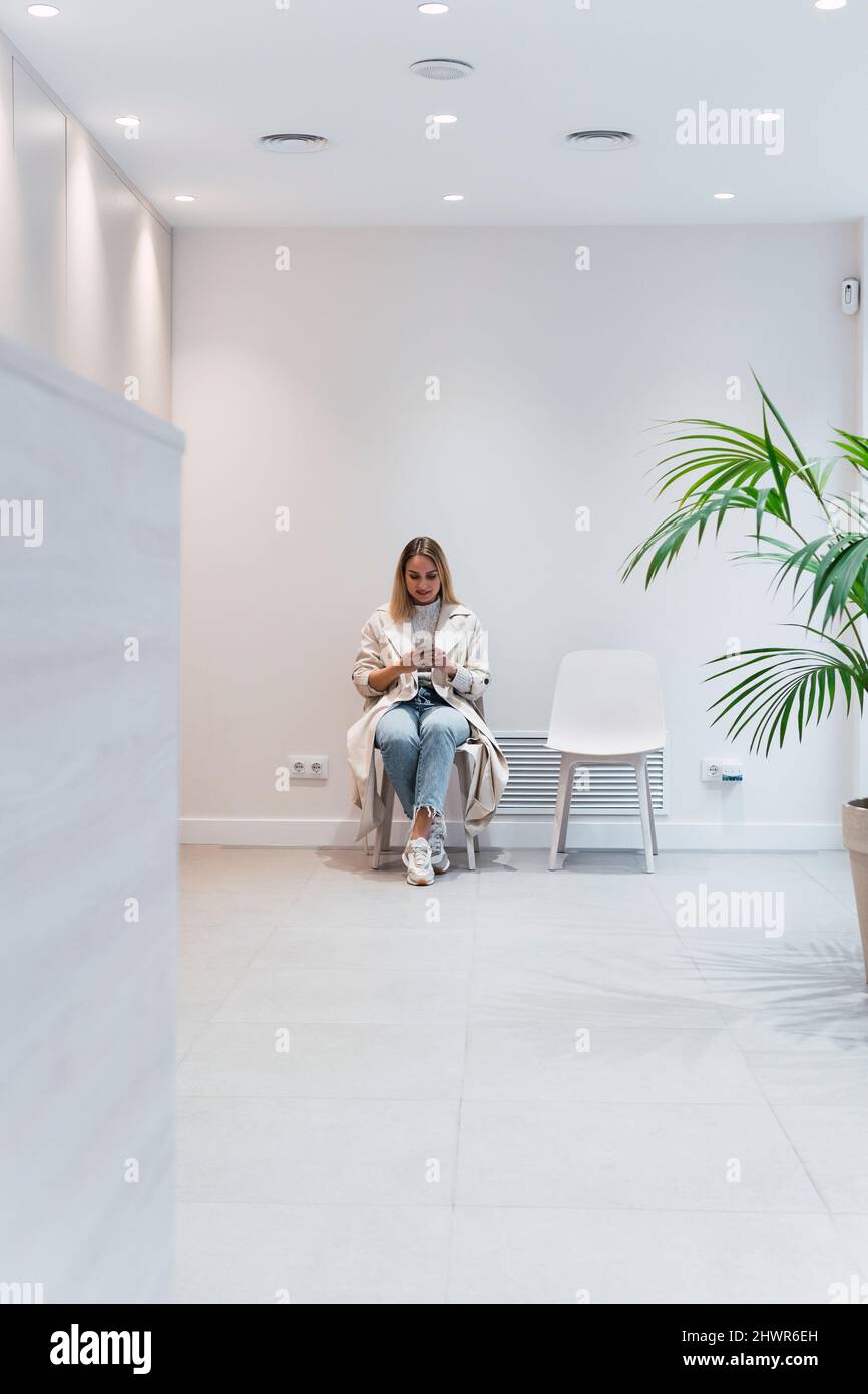 Donna che usa lo smartphone seduto in sala d'attesa presso la clinica Foto Stock