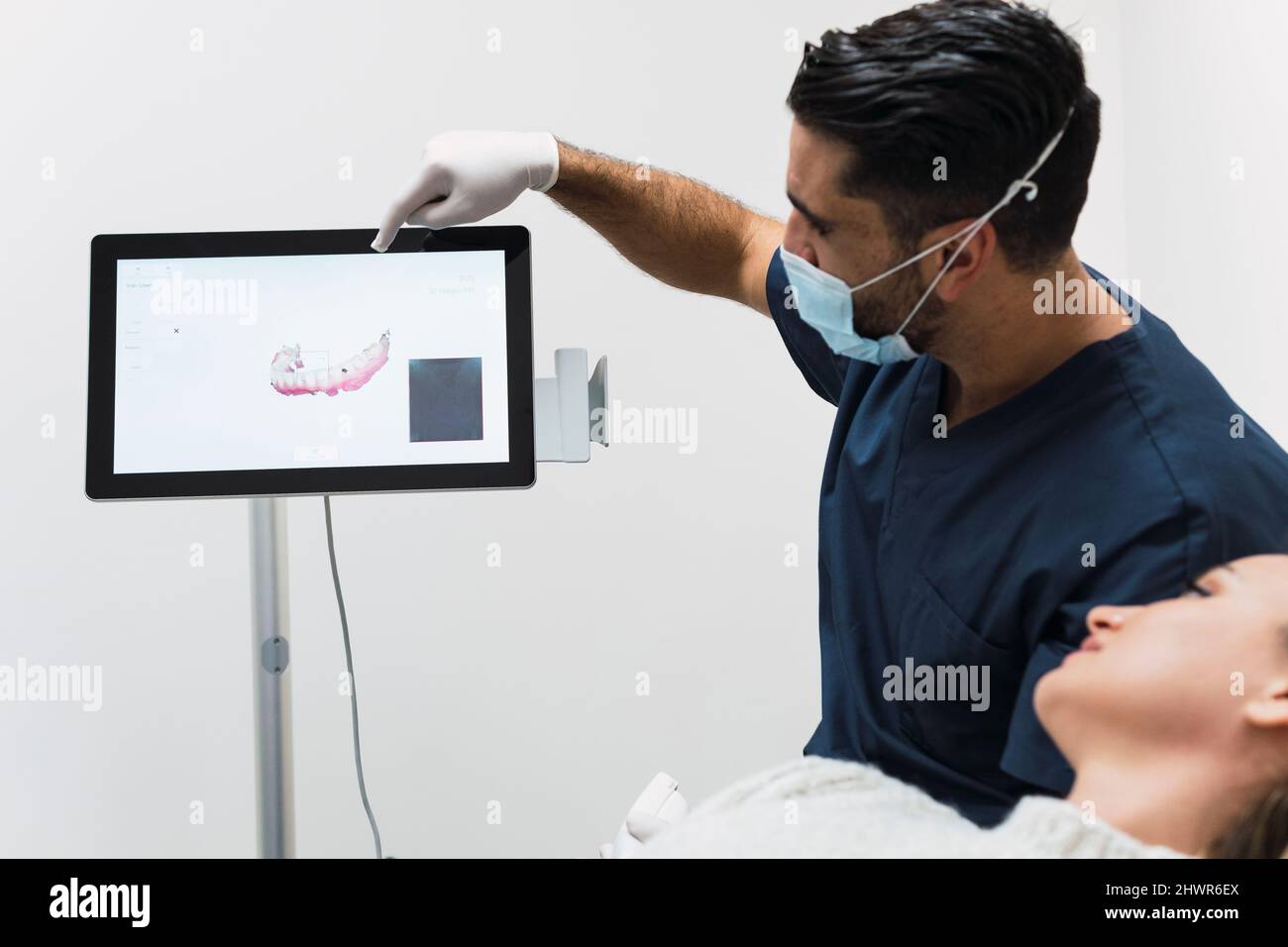 Dentista che mostra i raggi X dei denti al paziente sullo schermo dello scanner intraorale in clinica Foto Stock