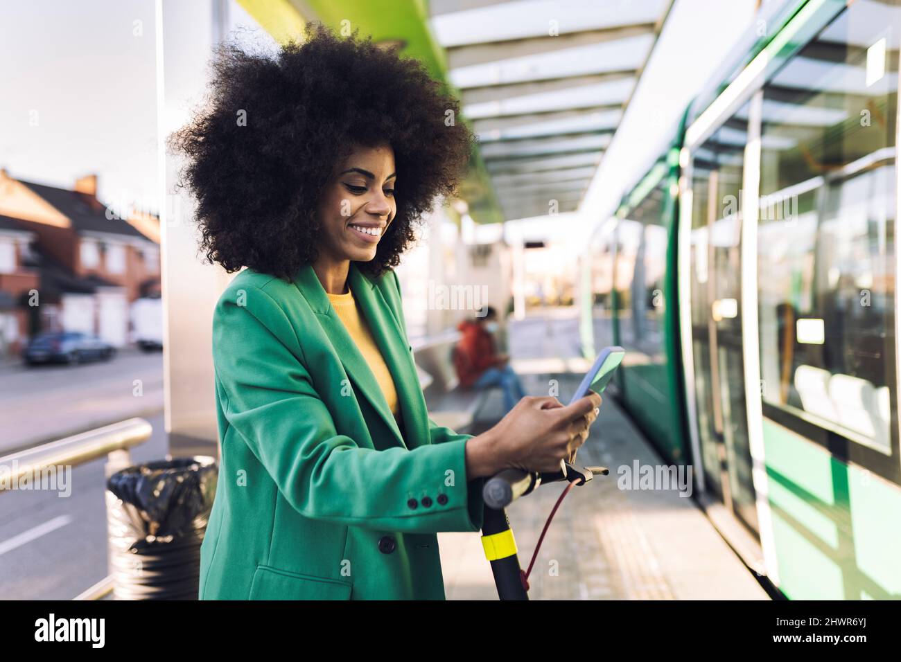 Donna d'affari sorridente che usa il telefono cellulare alla stazione del tram Foto Stock