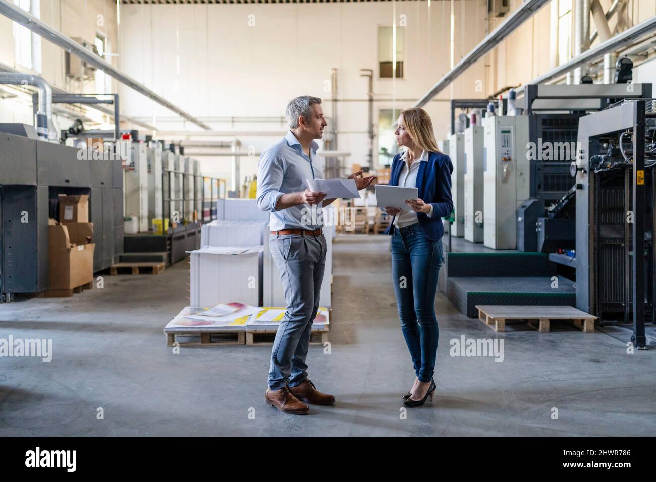 Uomo d'affari e donna d'affari che condividono idee in piedi in fabbrica Foto Stock