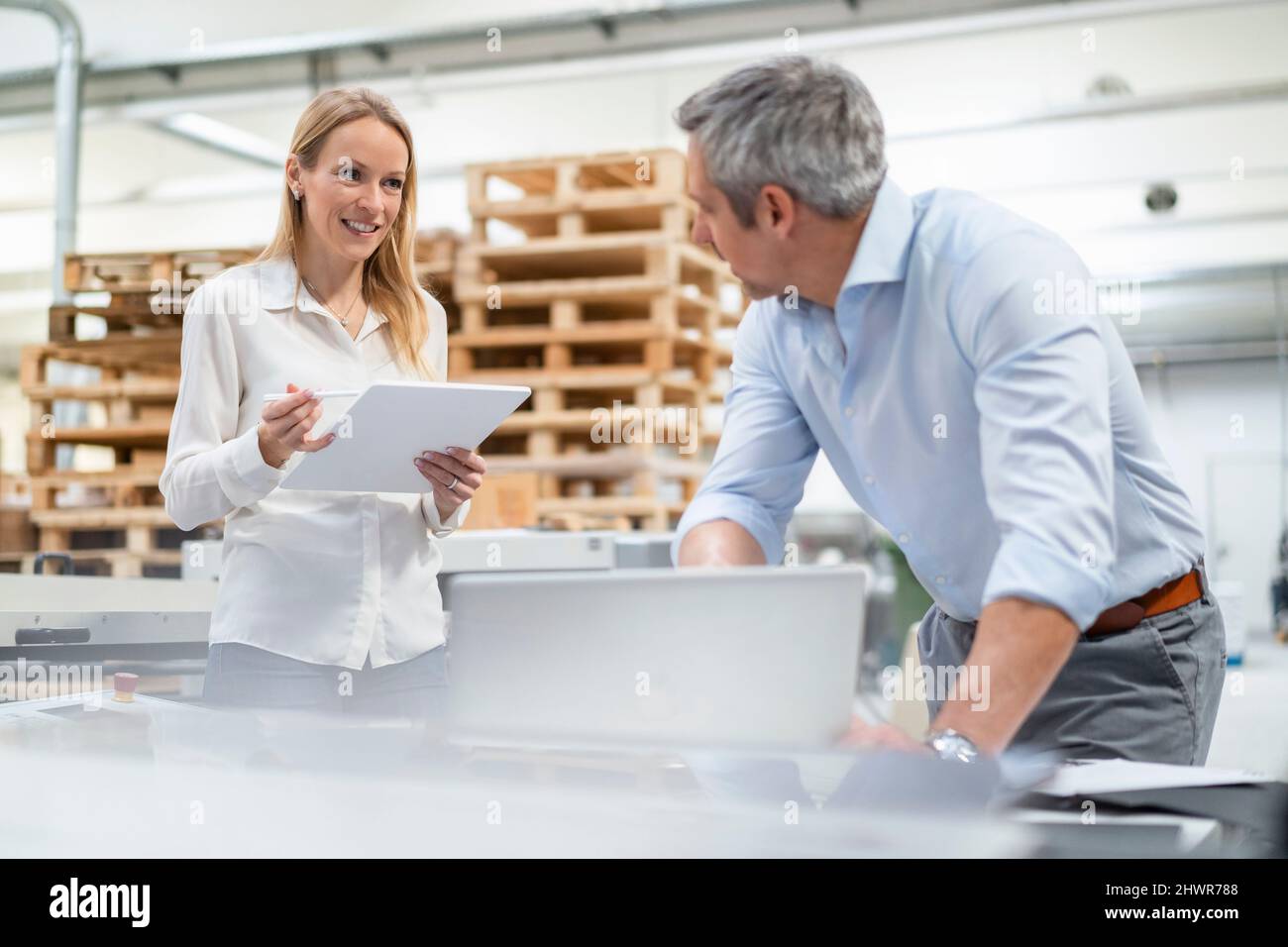 Donna d'affari bionda sorridente che tiene un tablet PC condividendo idee con un uomo d'affari nel settore Foto Stock