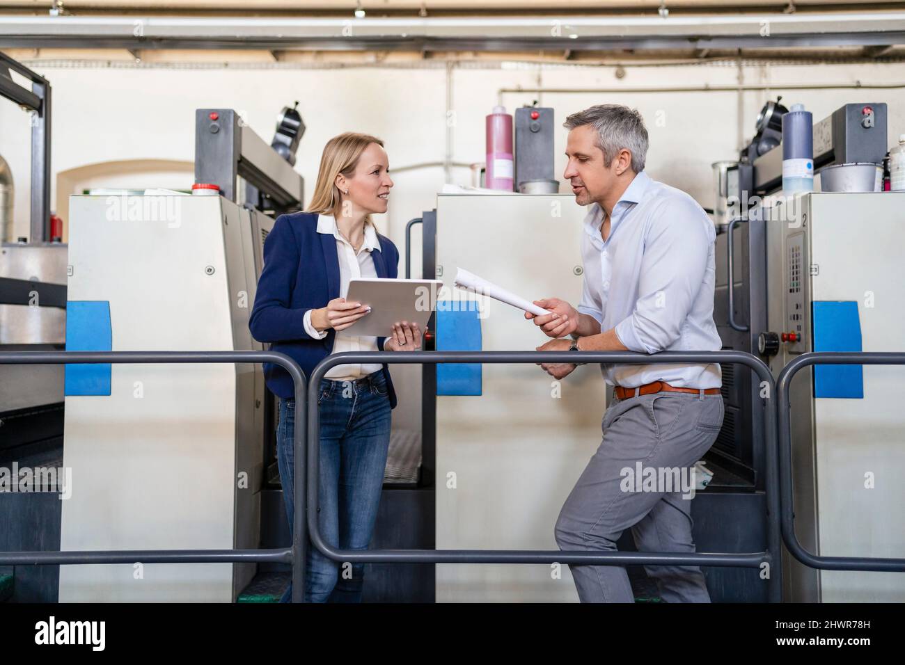 Uomo d'affari che condivide idee con una donna d'affari che tiene un tablet PC in fabbrica Foto Stock