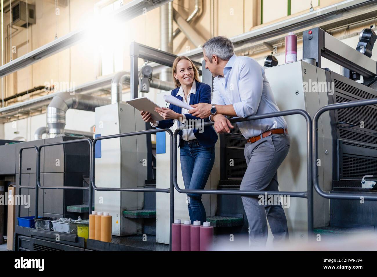 Sorridente donna d'affari bionda condividere idee con l'uomo d'affari in fabbrica Foto Stock