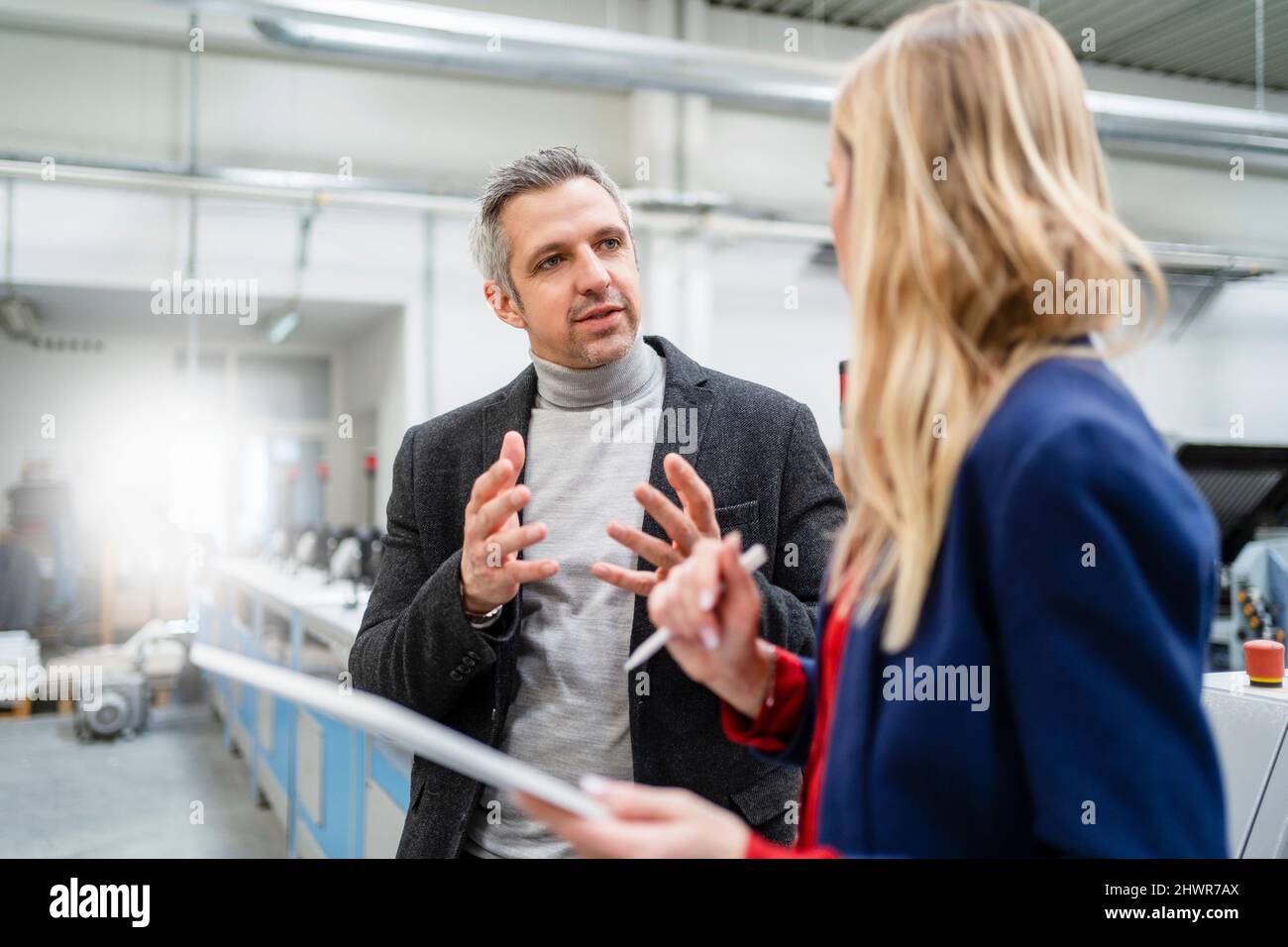 Uomo d'affari che condivide le idee con la donna d'affari bionda in fabbrica Foto Stock