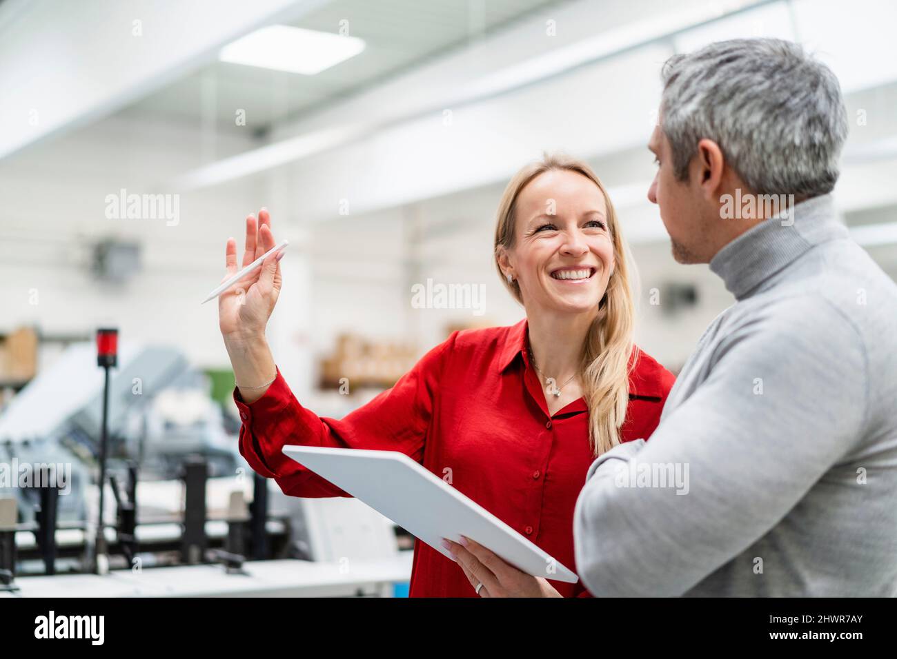 Donna d'affari allegra con PC tablet che condivide idee con colleghi in fabbrica Foto Stock