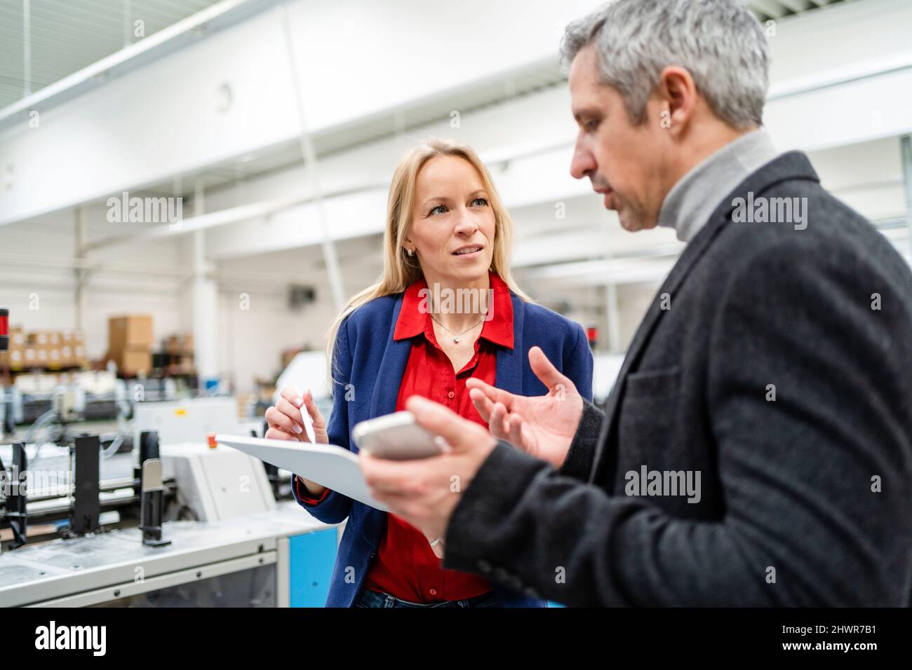 Donna d'affari bionda che guarda il collega che discute le idee in fabbrica Foto Stock