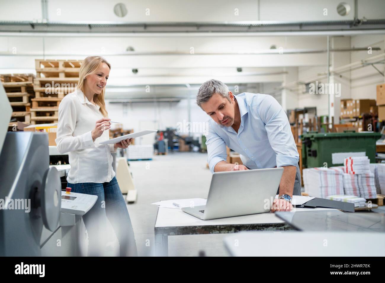 Uomo d'affari che parla di idee sul notebook con un collega in fabbrica Foto Stock