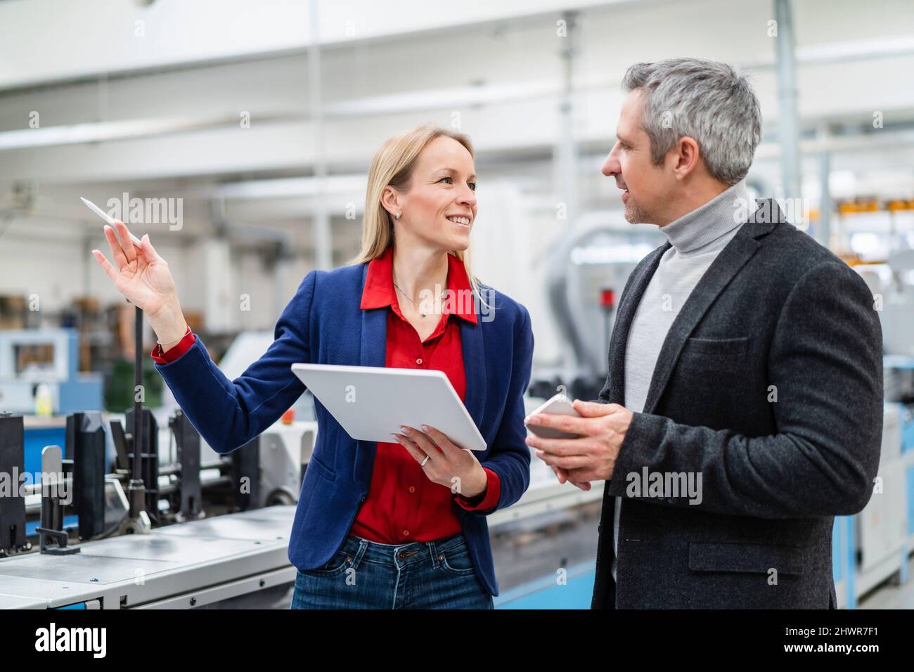 Donna sorridente con tablet PC che parla di idee con un collega in fabbrica Foto Stock