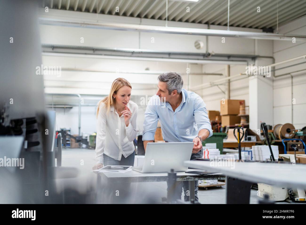 Uomo d'affari che guarda un collega che discute idee alla scrivania in fabbrica Foto Stock