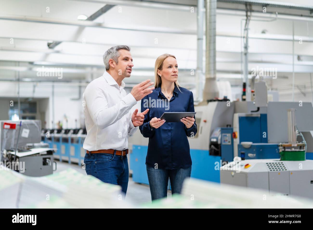 Uomo d'affari che condivide idee con una donna d'affari che tiene un tablet PC in fabbrica Foto Stock