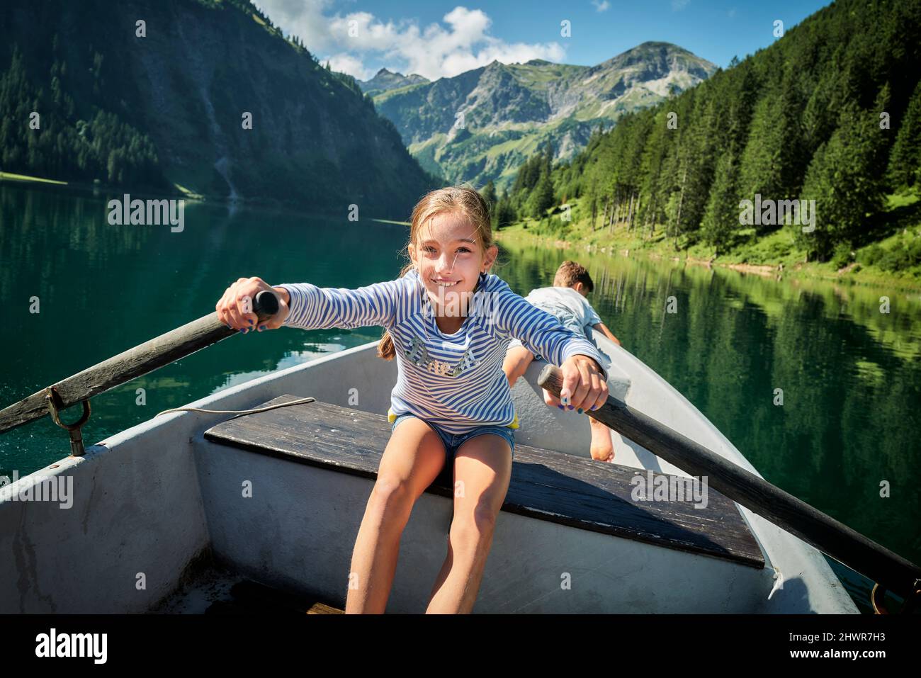 Ragazza sorridente remi barca con fratello in background Foto Stock