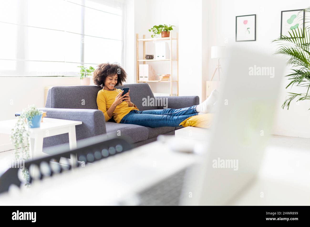 Donna sorridente che naviga in rete attraverso il telefono cellulare in soggiorno Foto Stock